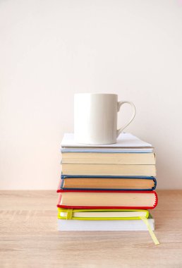 Üstünde beyaz bir fincan kahve olan bir yığın ciltli kitap..
