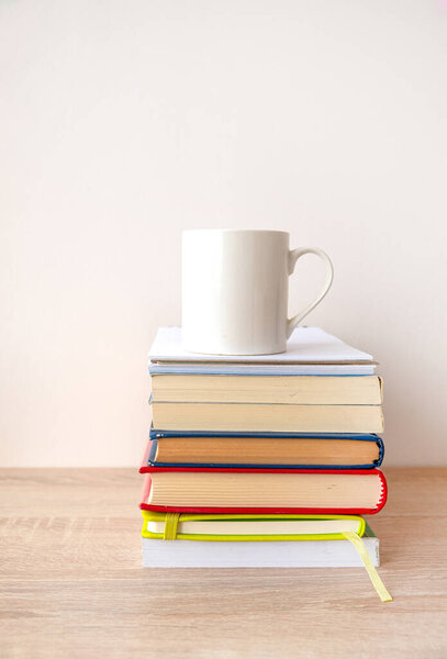 Stack of hardcover books with a white cup of coffee on the top.