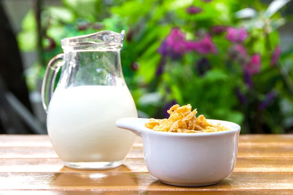 Corn flakes in white bowl and milk on wooden table — Stock Photo, Image