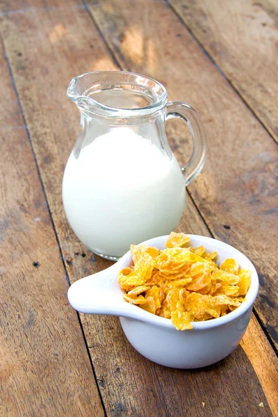 Copos de maíz en tazón blanco y leche en mesa de madera —  Fotos de Stock