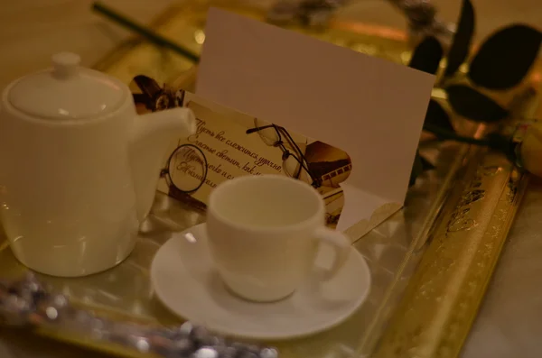 Image rapprochée d'une petite théière blanche avec une tasse, une carte postale et une rose sur le plateau — Photo