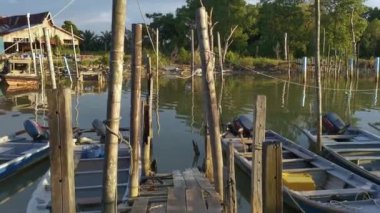 POV, eski iskele balıkçı köyü ve mangrov ormanları arka planında park etmiş renkli ahşap balıkçı tekneleriyle ahşap köprüde yürüyor, Parit Jawa, Malezya