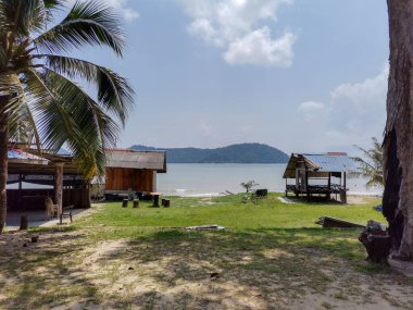 Çimenli bir plajda kumdan bir çardak, mavi gökyüzü, deniz dalgası, arka planda palmiye ağacı. Tropik plaj. Güzel sahil. Şehir tatili. Doğada keyifli bir hafta sonu.