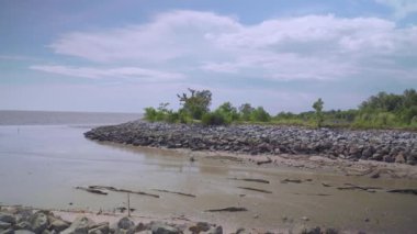 Panning shot from tidal to tropical forest and rock stone blue sky with clouds. Sandy shallow water near the shore beach in sunny summer day. Coast at low tide