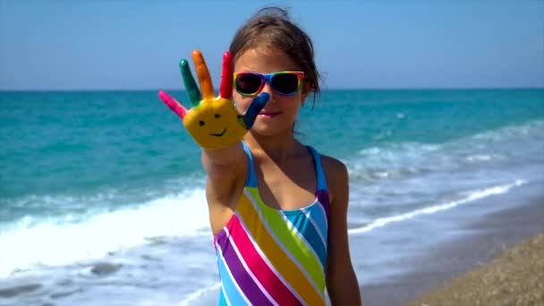 Ett barn vid havet med färger på händerna ett leende. Selektiv inriktning. — Stockvideo