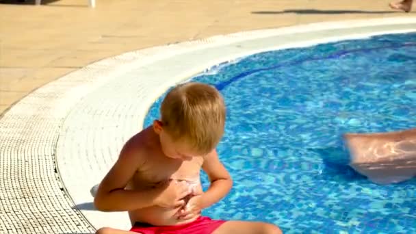 Uma criança mancha protetor solar junto à piscina. Foco seletivo. — Vídeo de Stock