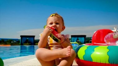 Çocuk havuzun yanında bir karpuz yiyor. Seçici odak.