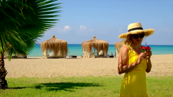 Μια γυναίκα με καπέλο και φόρεμα περπατάει στην παραλία. Επιλεκτική εστίαση. — Αρχείο Βίντεο