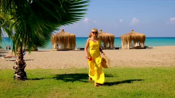 Una mujer con sombrero y vestido camina por la playa. Enfoque selectivo. — Vídeo de stock
