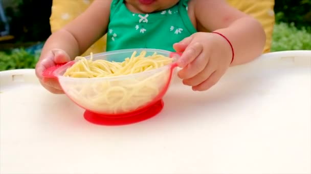 Baby eats spaghetti herself. Selective focus. — Stock Video