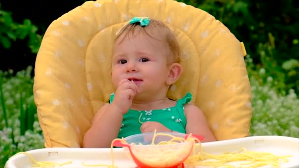 Baby eats spaghetti herself. Selective focus. — Stock Video