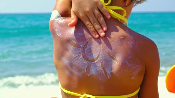 The child puts sunscreen on her back. Selective focus. — Stock video