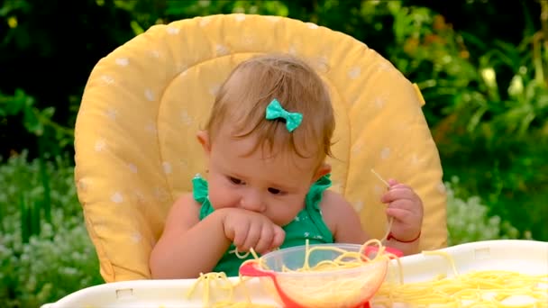 Baby eats spaghetti herself. Selective focus. — Stock Video