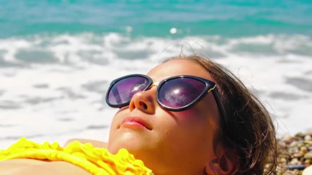 Et barn solbader på stranden i solbriller. Selektivt fokus. – Stock-video