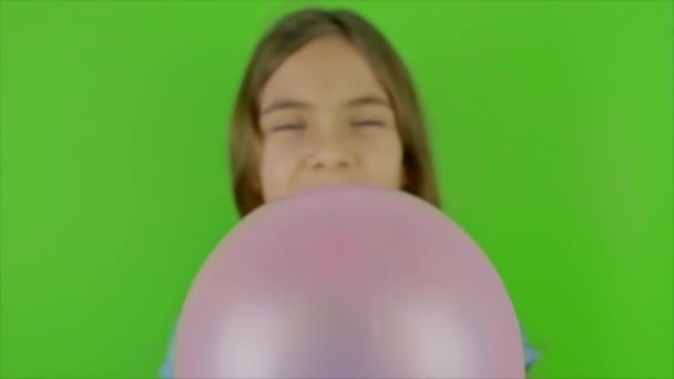 Un enfant souffle un ballon sur un fond vert. Concentration sélective. — Video