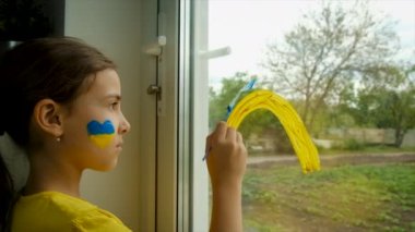 Bir çocuk evin camına Ukrayna gökkuşağı çiziyor. Seçici odaklanma. Çocuk.