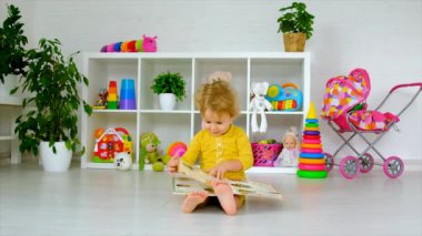 The child is looking at a book in the room. Selective focus. Kid.