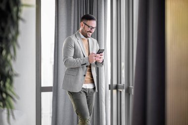 Ofiste sıradan giyinmiş gülümseyen adam. Elinde cep telefonu olan bir iş adamı. Ofiste telefonla gülümseyen bir işadamı. Cep telefonuna bakıp gülümseyen küçük bir girişimci..