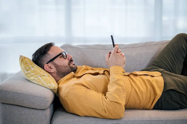 Young Adult Mature Man Using Smart Phone Resting Lying Sofa — Stock fotografie