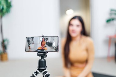 Genç kadın fitness eğitmeni blog yazarı etkileyicisi video blogu konseptini kaydediyor tripodlu sosyal medya vlog yazıcısında akıllı telefona bakarak cep telefonuyla video yayınını çekiyor