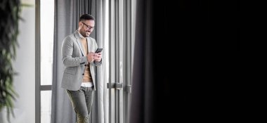 Ofiste sıradan giyinmiş gülümseyen adam. Elinde cep telefonu olan bir iş adamı. Ofiste telefonla gülümseyen bir işadamı. Cep telefonuna bakıp gülümseyen küçük bir girişimci..