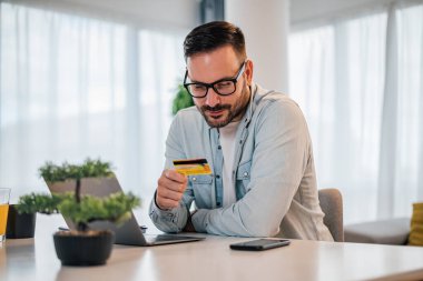 İnternet üzerinden alışveriş yapan ya da ofisinden ya da ofisinden online ödeme yapan memnun genç bir adam.