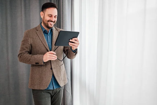 Uśmiechnięty Biznesmen Casualach Stojący Biurze Przy Oknie Przy Użyciu Tabletu — Zdjęcie stockowe