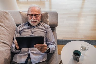 Üst düzey yakışıklı adam evindeki ya da ofisindeki kanepeye uzanmış el bilgisayarı kullanarak arkadaşlarına ve ailesine hediye alıyor ya da internetten video görüşmesi yapıyor.