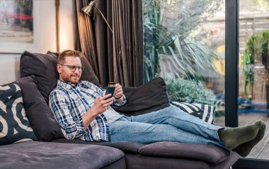 Sakin yetişkin bir adam, koltuğunda oturmuş, aylık bütçesine, akıllı telefonuna bakıyor..