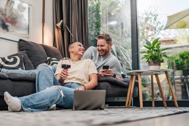 Neşeli kısa saçlı kadın, şarap içiyor, sakallı ortağına bakıyor..