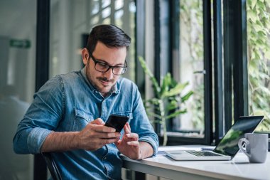 Sakallı adam, günlük programını kontrol ediyor, cep telefonundan..