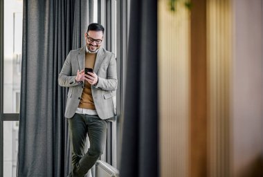 Sırıtan sakallı, yetişkin bir adam, cep telefonunda dokunmatik ekran kullanıyor..