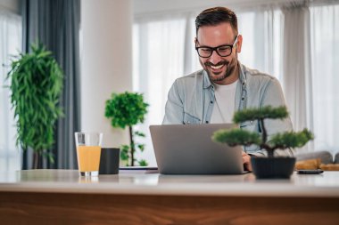 Smiling male business professional using laptop. Confident entrepreneur sitting at desk in office. He is wearing smart casuals at workplace.