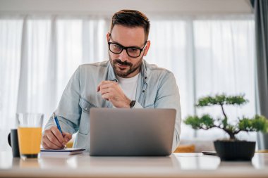 Not defterine iş dünyasının kendine güvenen profesyonel fikirleri. İşadamı dizüstü bilgisayar üzerinde çalışırken strateji planlıyor. Ofisteki masada oturuyor..