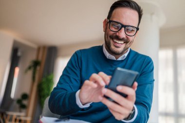 Akıllı telefondaki neşeli girişimci şebekesi. Kablosuz teknolojiyi kullanan erkek profesyonellere yakın çekim. İş yerinde şık kıyafetler giyiyor..