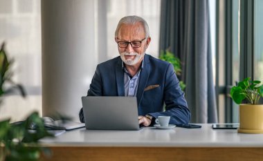 Dizüstü bilgisayarda çalışan kendinden emin bir iş adamı. Gözlük takan yaşlı erkek yönetici kablosuz bilgisayar kullanıyor. O, ofiste masa başında otururken formalitelerde..