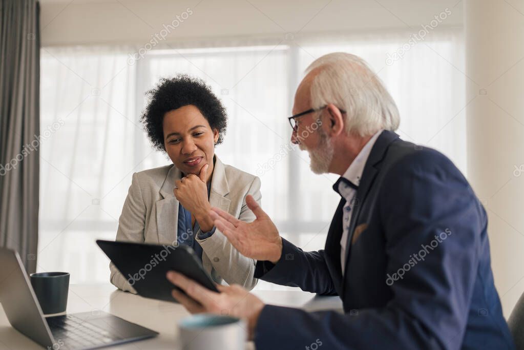 Senior businessman discussing with female colleague over digital tablet, Professionals are planning strategy in meeting at desk, They are sitting in corporate office.