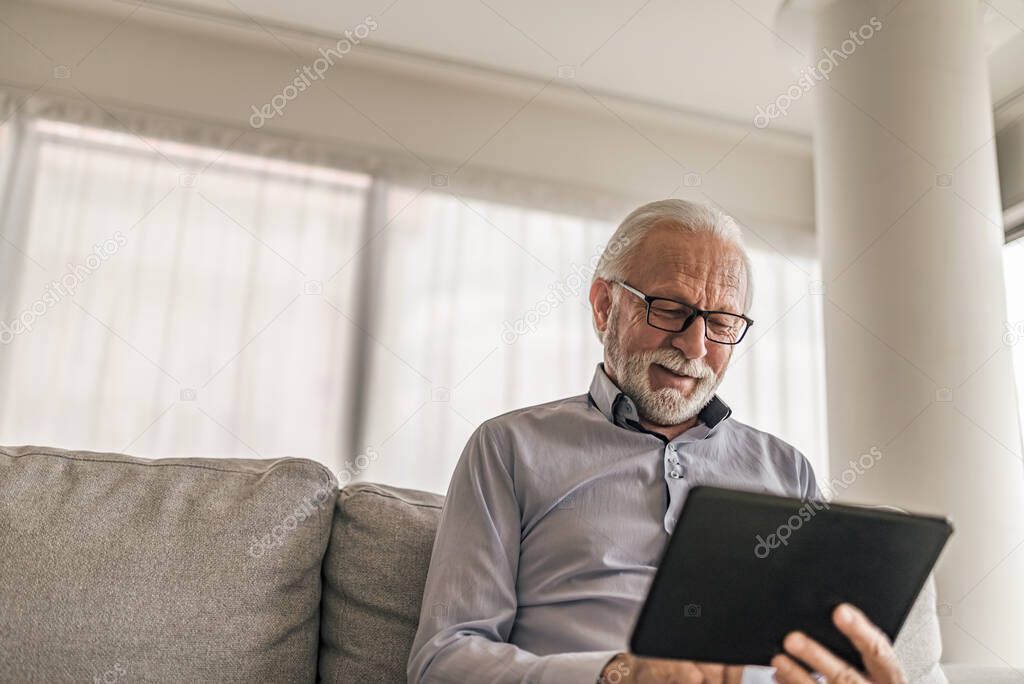 Confident senior businessman using digital tablet, Male professional is wearing formals, He is using wireless computer while sitting on sofa at office.