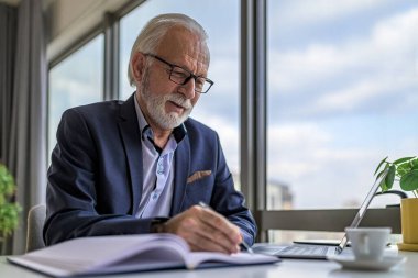 Dizüstü bilgisayarda çalışan ciddi bir iş adamı. Kıdemli işadamı ofiste masa başında oturuyor. İş yerindeki ofisinde gözlük takıyor..