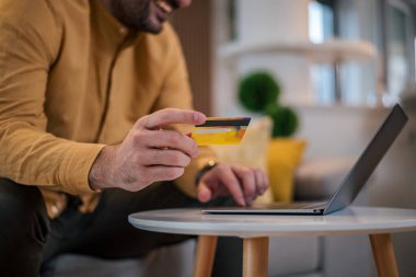 Kredi kartı tutan ve dizüstü bilgisayarı online alışveriş kavramını kullanan adam alışverişini kapatan internet üzerinden yazıcı bilgilerini kontrol eden internet bankacılığı hizmetleri ödemelerini yapan