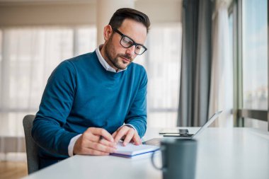 Günlükte ciddi bir profesyonel iş planı var. Erkek profesyonel masabaşında çalışıyor. Kurumsal ofiste şık kıyafetler giyiyor..