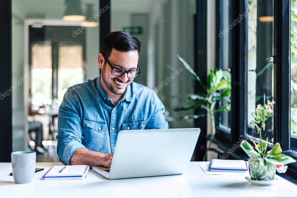 Smiling young entrepreneur working on laptop at table. Confident male professional is analyzing success plan. He is sitting at home office.