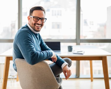 Portrait of young smiling happy handsome successful businessman entrepreneur freelancer working from home office or business office on laptop computer looking at camera.