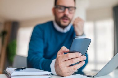 Cep telefonundan sıkılmış iş adamının mesajlarına yakın çekim. Genç erkek yönetici ofiste masasında oturuyor. Akıllı telefona odaklan..