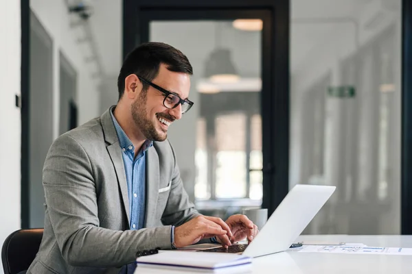 Smiling young man working on laptop in modern office, checking email in the morning, writing message on social network. Happy young male using internet banking service, searching information.