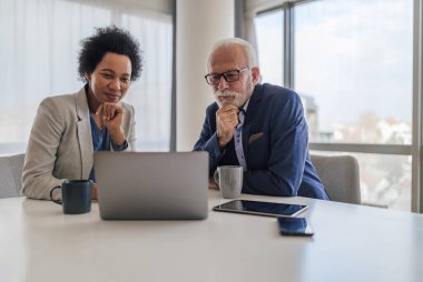 Focused male and female partners analyzing business plan on laptop. Colleagues sitting with hand on chin during meeting at desk. They are brainstorming in office.