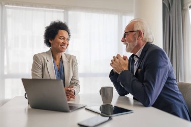 Confident businesswoman discussing business plan with senior partner. Male and female professionals planning strategy during meeting. They are sitting at desk in office.