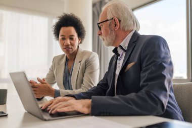 Serious male and female executive discussing business plan on laptop. Business partners brainstorming during meeting at desk. They are sitting in corporate office.
