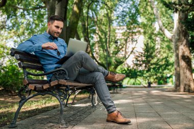 Dizüstü bilgisayar kullanan kendine güvenen genç bir iş adamı. Form giyen profesyonel bir erkek bankta oturuyor. O, şehirdeki parkta çalışıyor..