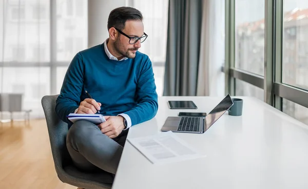 Serious male manager making notes in diary. Young entrepreneur is planning strategy while working at desk. He is wearing smart casuals in office.